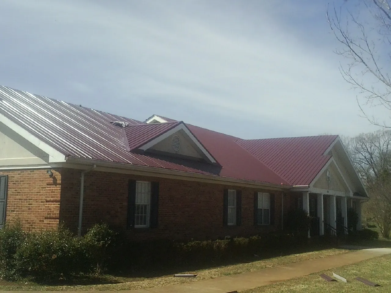 Red metal roof with gabled entries on a long brick building, from a Hail Damage Roof Repair job in Steilacoom