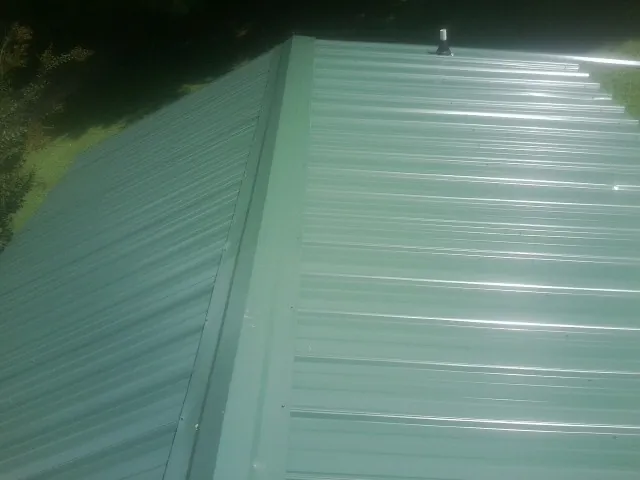 New green metal panels meeting at the ridge of a roof — Flat Roof Repair work by our crew in Steilacoom