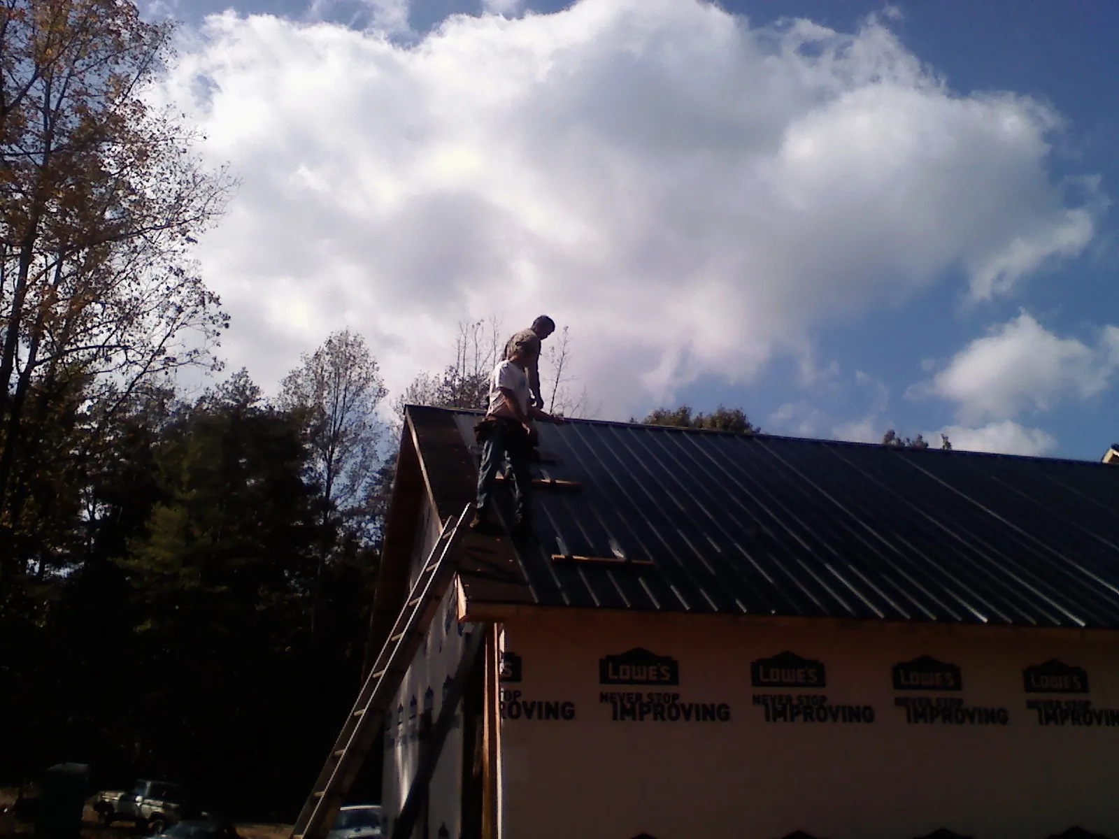 Roofer fastening dark metal panels high against a cloudy sky, from a Roof Inspection job in Steilacoom
